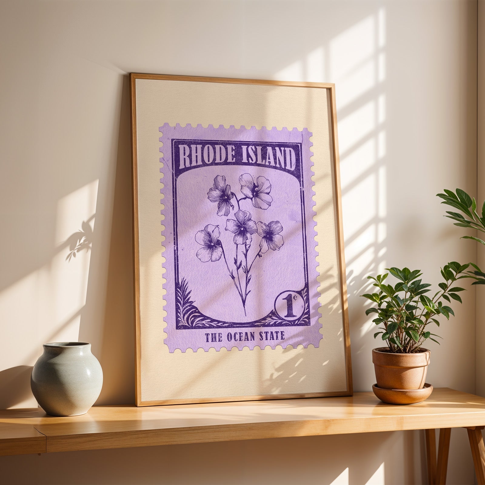 Rhode Island Violet stamp print in a light oak frame leaning on a wooden table beside a stoneware vase