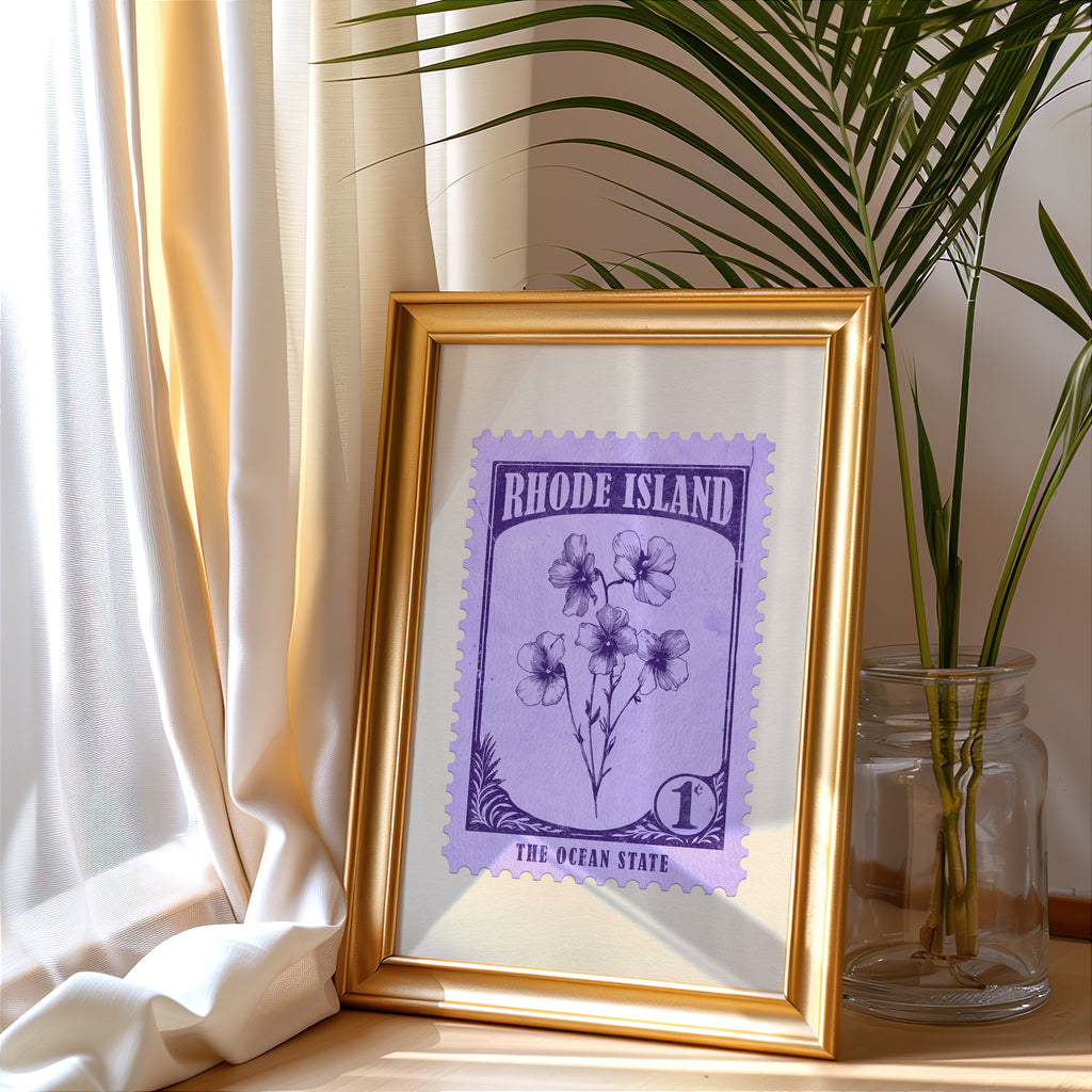 Rhode Island stamp print in a gold frame leaning by a cream curtain with a palm in a glass jar