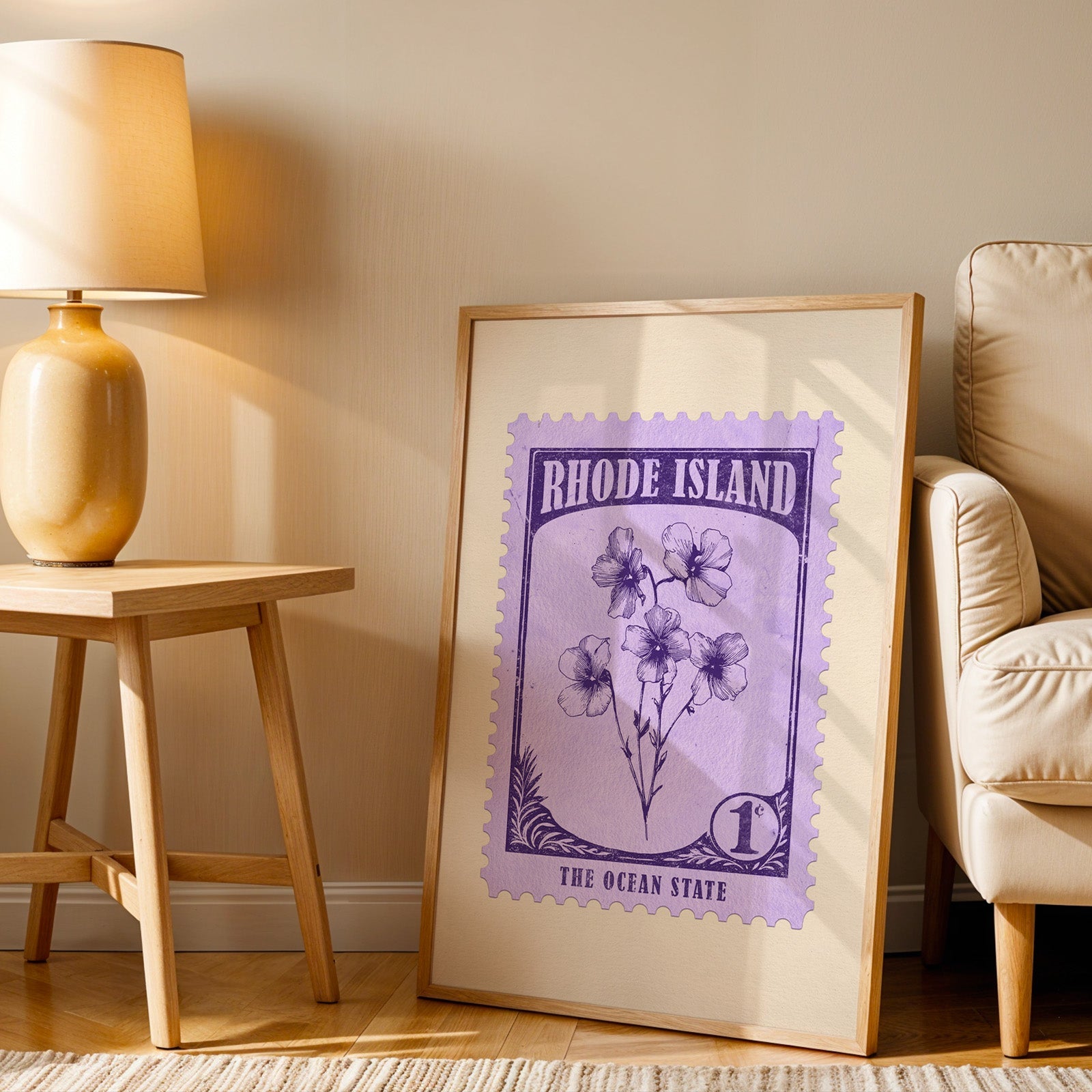 Rhode Island stamp print in a wood frame resting on the floor beside a beige armchair and a yellow lamp