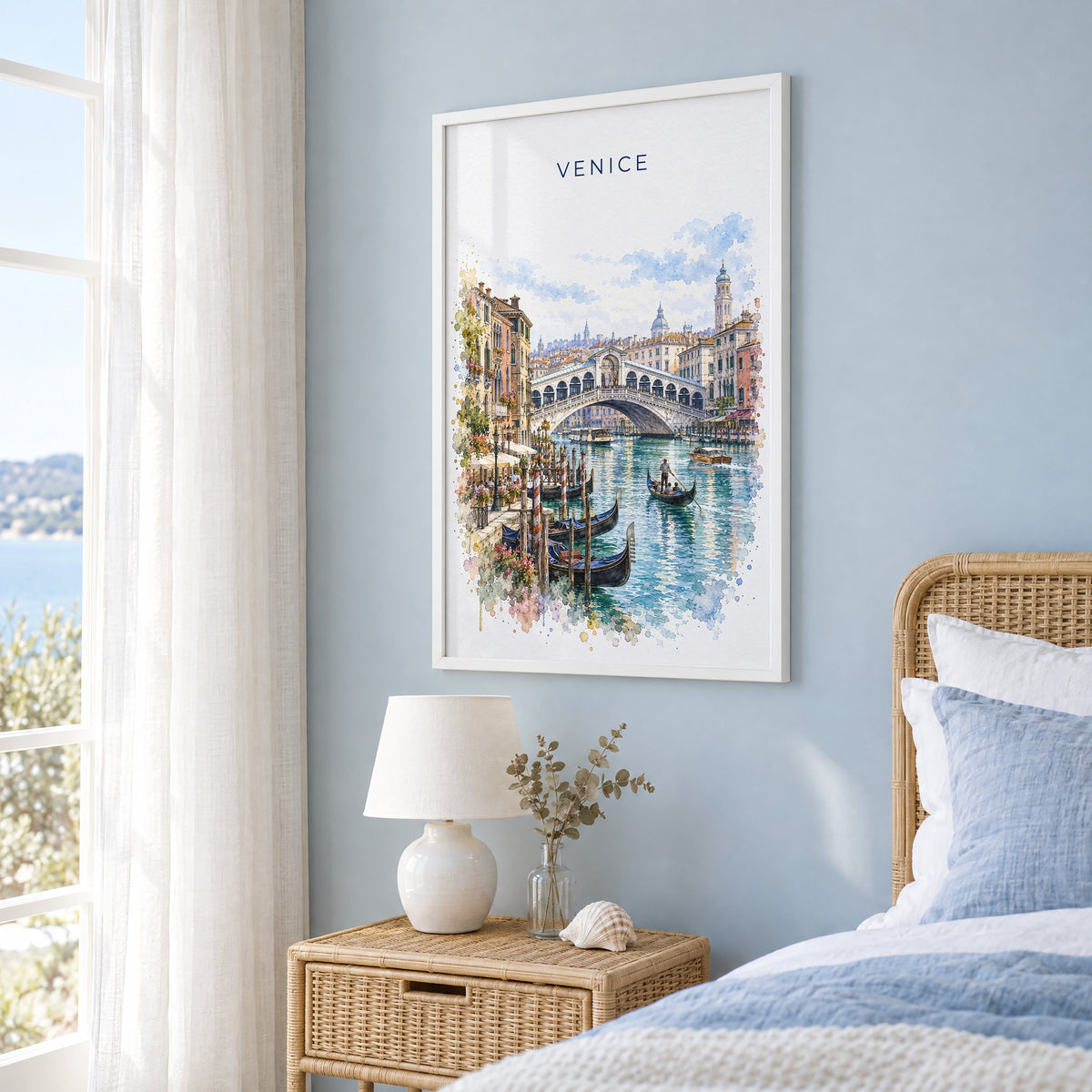 Rialto Bridge watercolor print in a white frame on a pale blue wall beside a rattan bed in a coastal bedroom