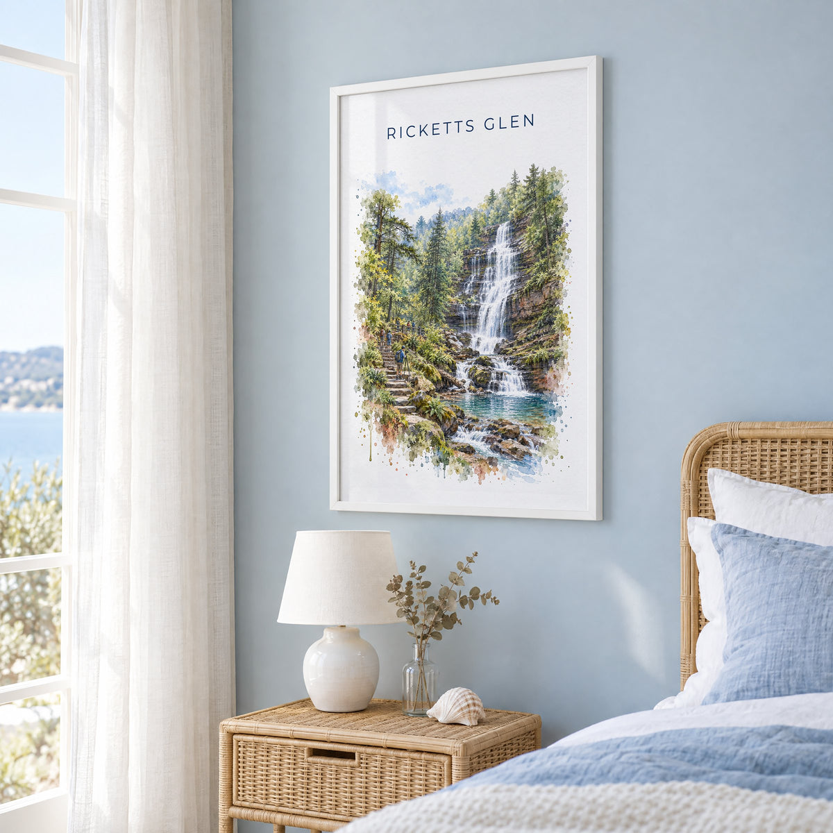 Ricketts Glen State Park watercolor print in a white frame on a pale blue wall beside a rattan bed in a coastal bedroom