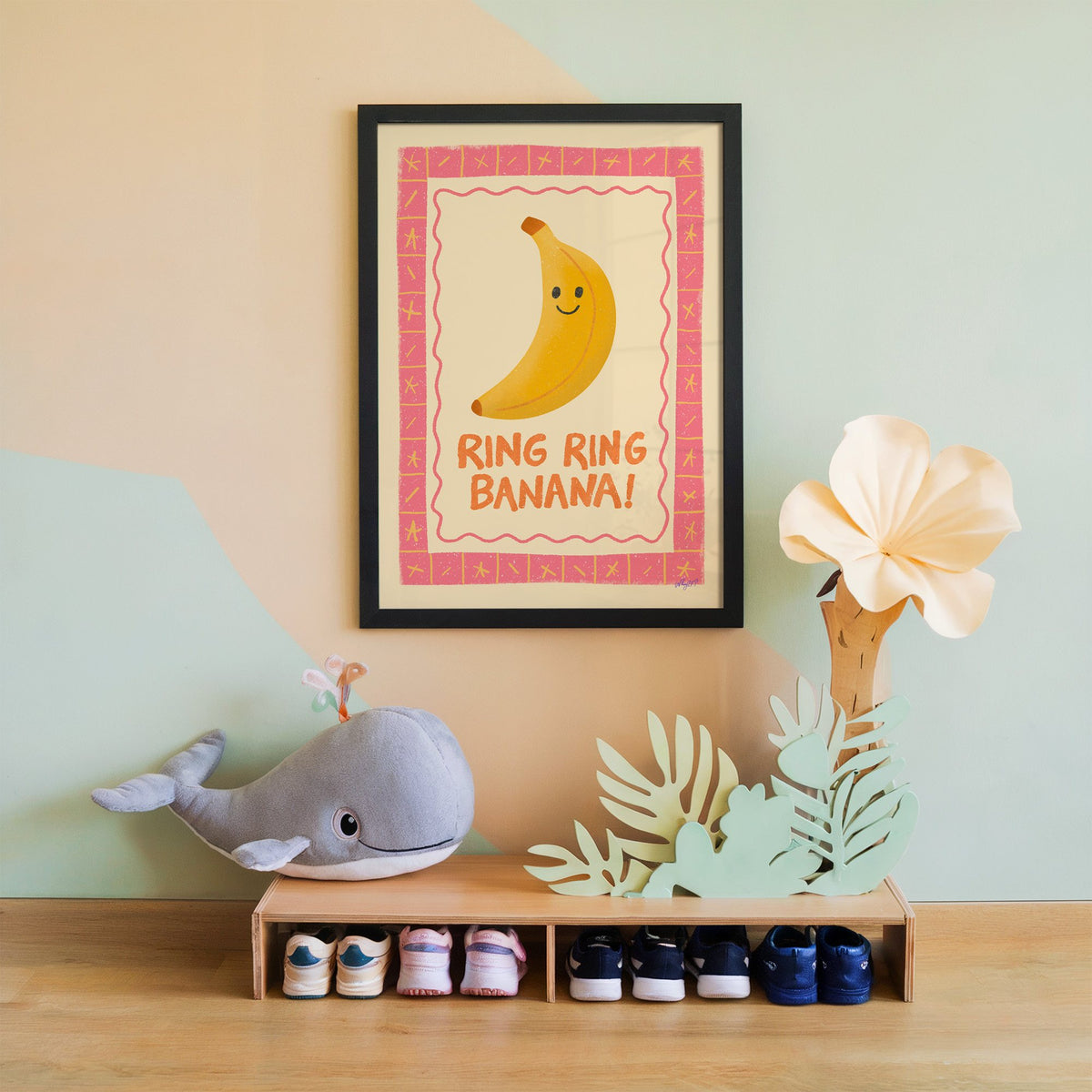Smiling banana pink border nursery print in a black frame on a mint and peach wall above a whale plush