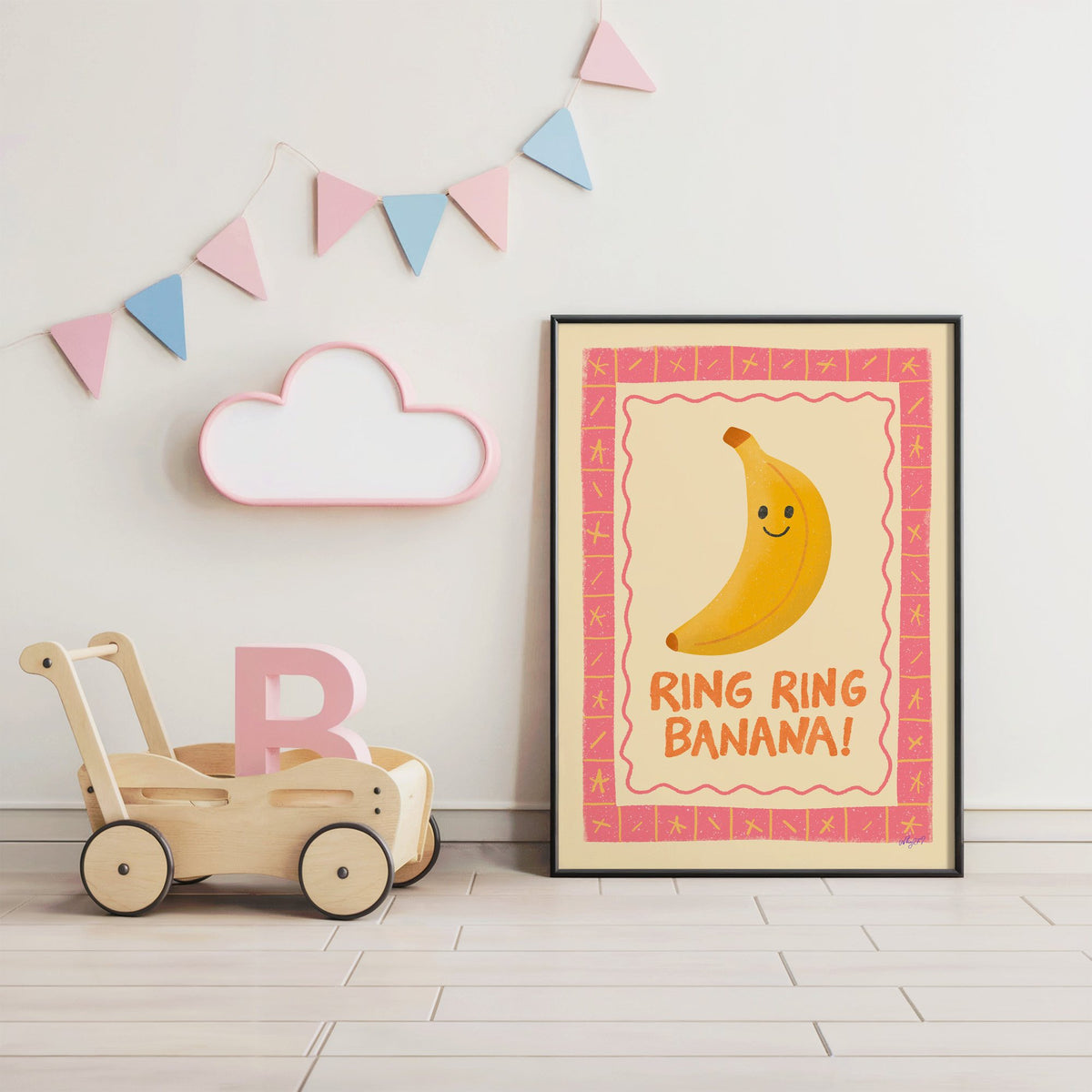 Smiling banana pink border nursery print in a black frame under pastel bunting by a wooden baby walker