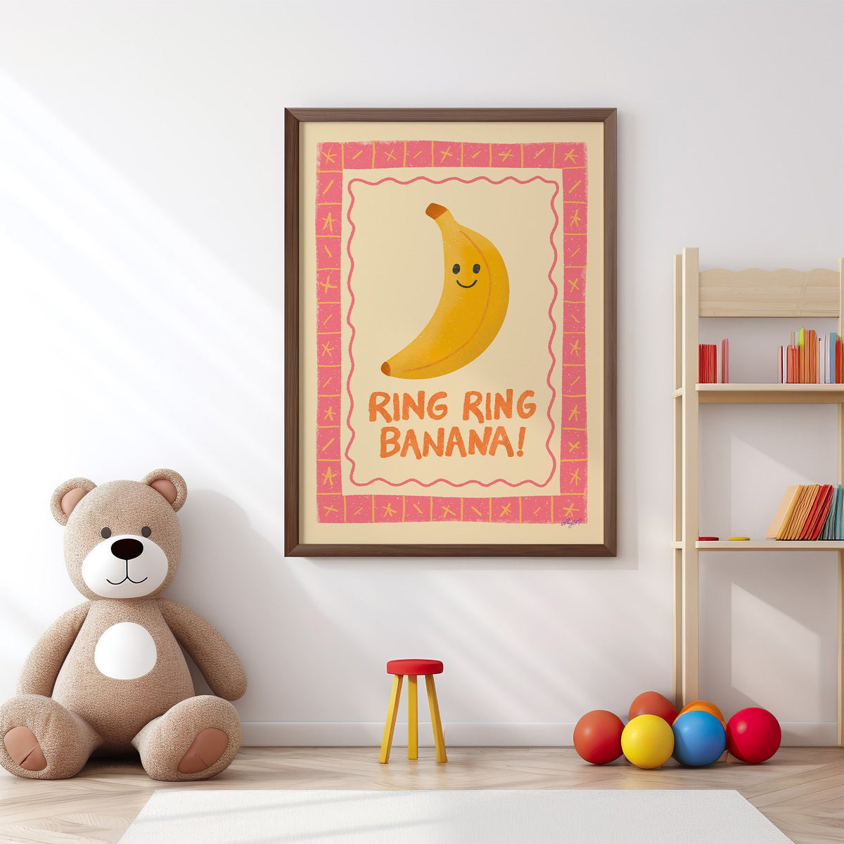 Smiling banana pink border nursery print in a walnut frame above a big teddy bear by a bookshelf