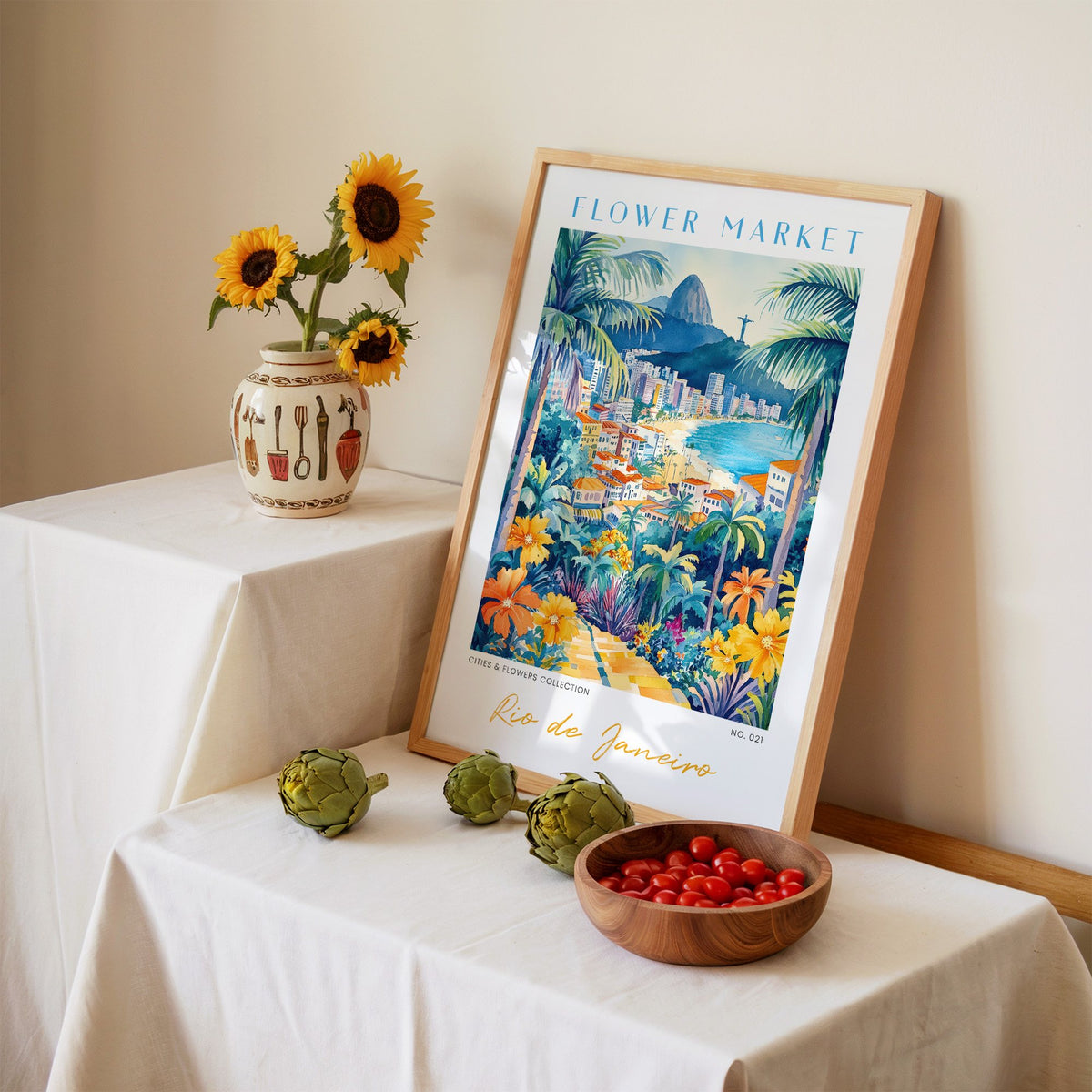 Rio de Janeiro flower market print in an oak frame leaning on a linen-draped table beside a vase of sunflowers