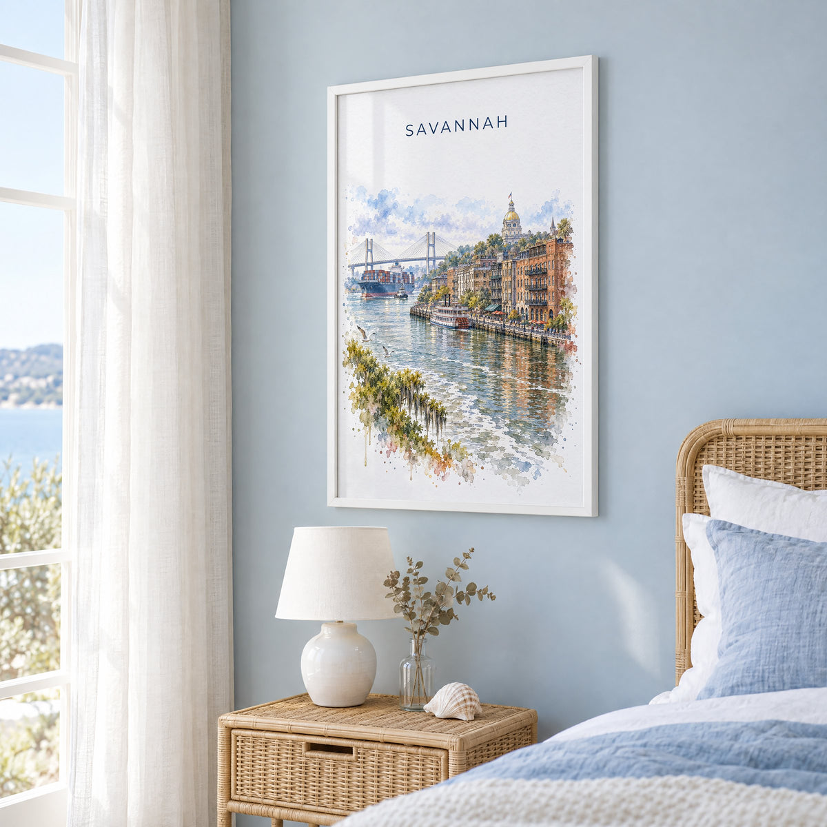 River Street Savannah watercolor print in a white frame on a pale blue wall beside a rattan bed in a coastal bedroom