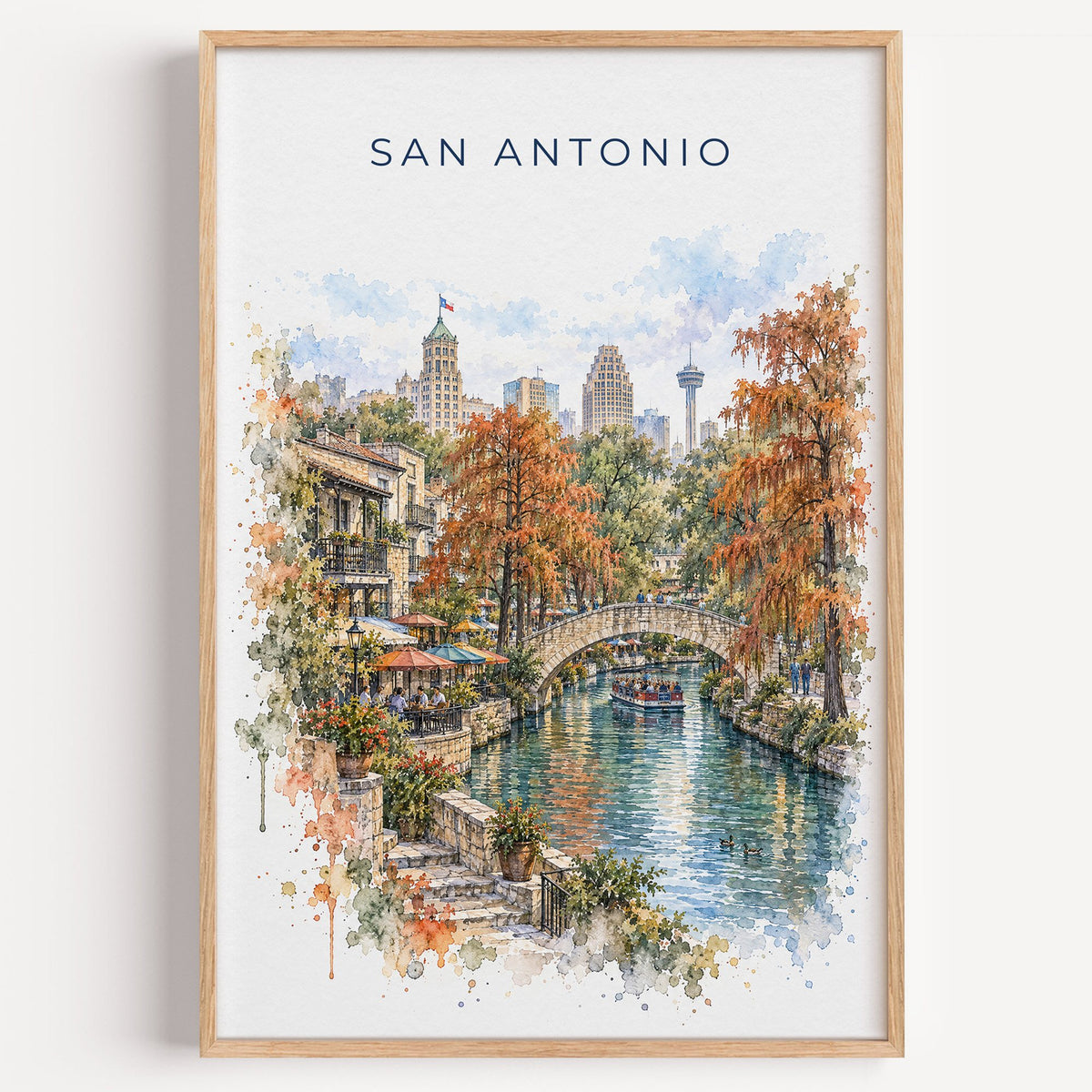 San Antonio River Walk watercolor print in a light oak frame on a plain white wall