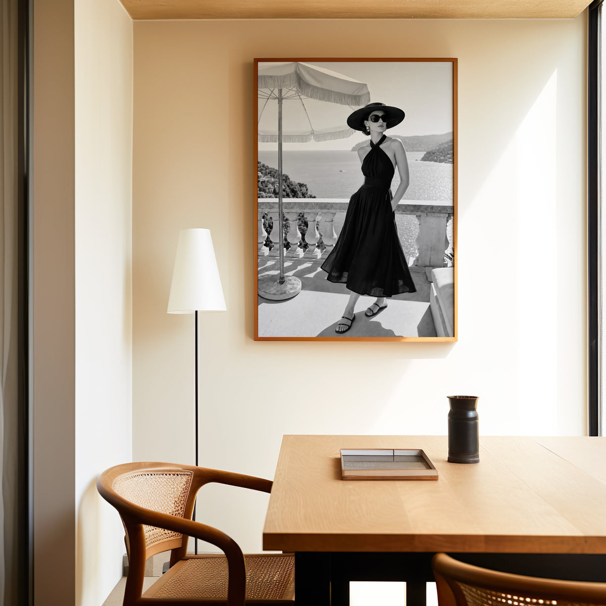 Black and white woman in halter dress on terrace print in an oak frame above a dining table and cane chair