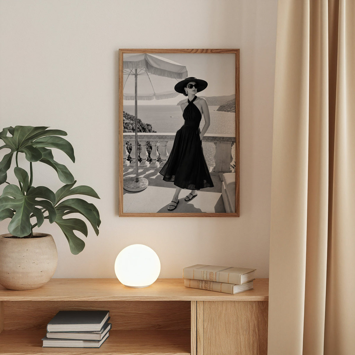 Black and white woman in halter dress on terrace print in a walnut frame above an oak cabinet with a glowing globe lamp