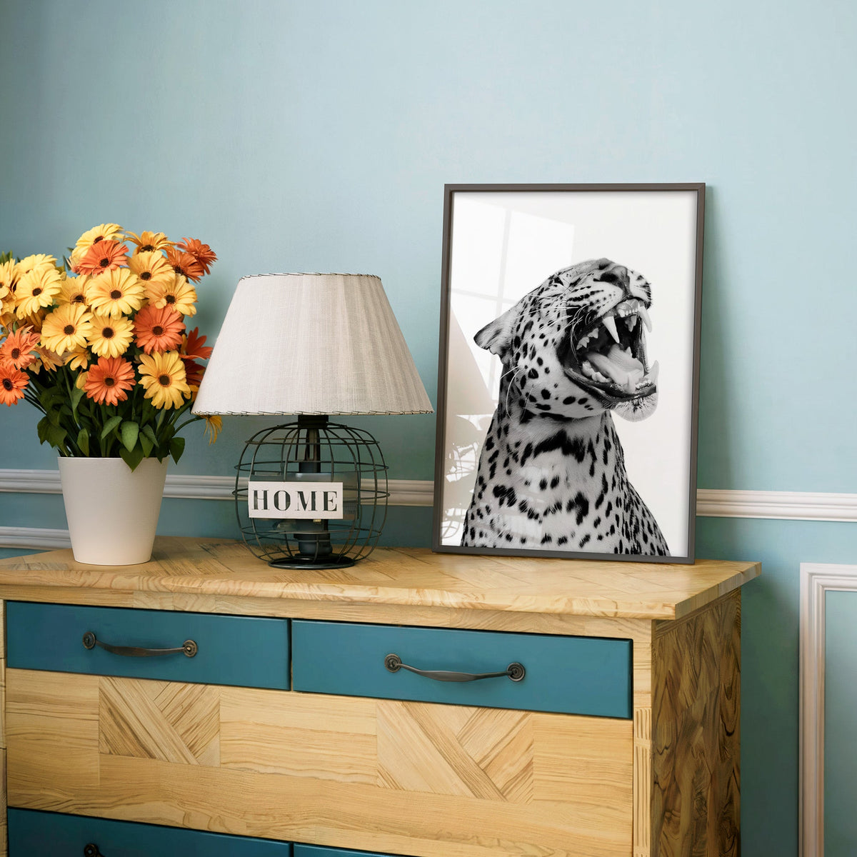 Roaring leopard portrait on white background print in a charcoal frame on a teal dresser beside orange daisies