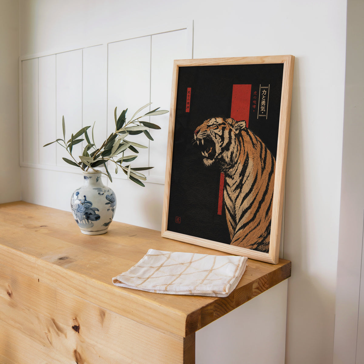roaring tiger on black with red banner print in a pine frame on a wooden counter beside a blue and white porcelain vase