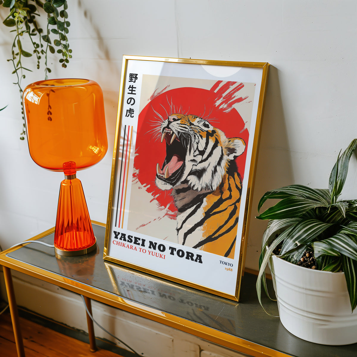 Roaring tiger with red sun print shown in a gold frame on a console beside an orange glass lamp