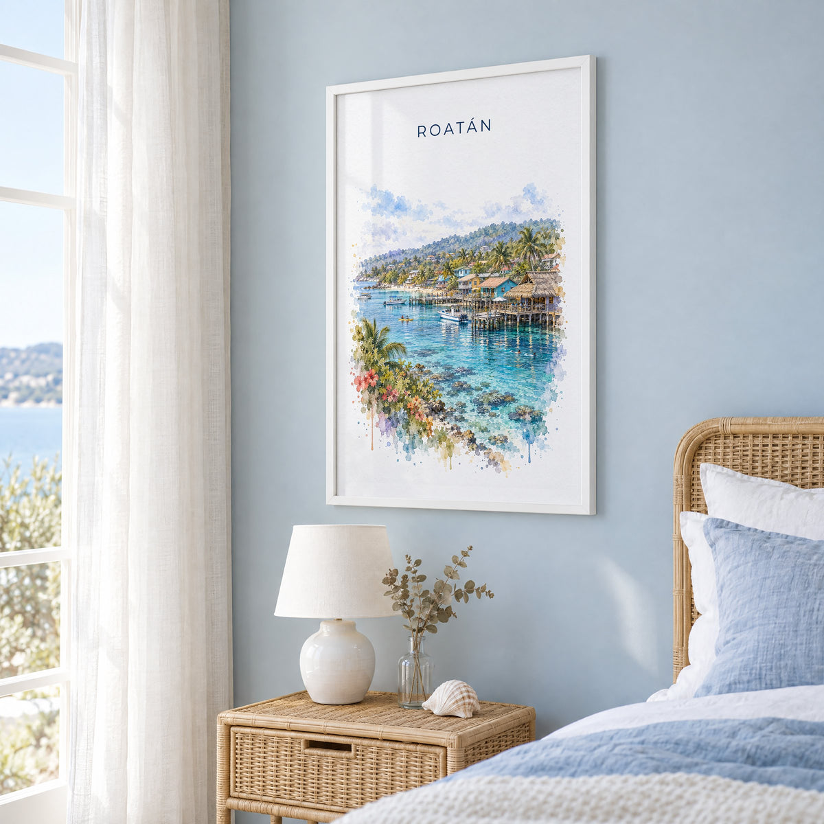 Roatan watercolor print in a white frame on a pale blue wall beside a rattan bed in a coastal bedroom