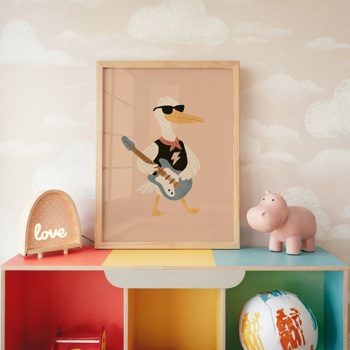 Pelican playing electric guitar nursery print in an oak frame on a rainbow toy shelf against cloud wallpaper