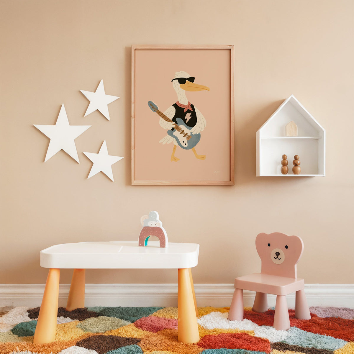 Pelican playing electric guitar nursery print in an oak frame on a peach wall above a kids table with wall stars
