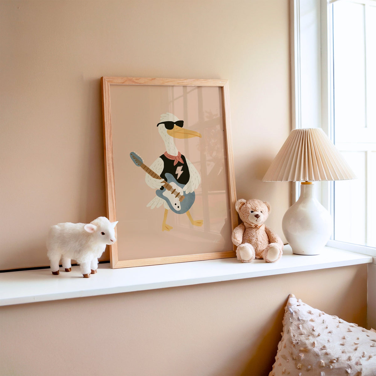 Pelican playing electric guitar nursery print in an oak frame on a window ledge with a toy lamb and teddy