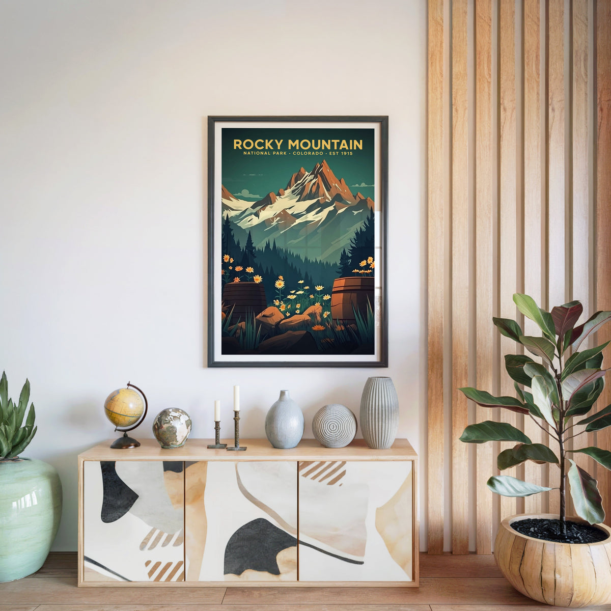 Rocky Mountain National Park print in a black frame above a light wood sideboard with a globe and vases