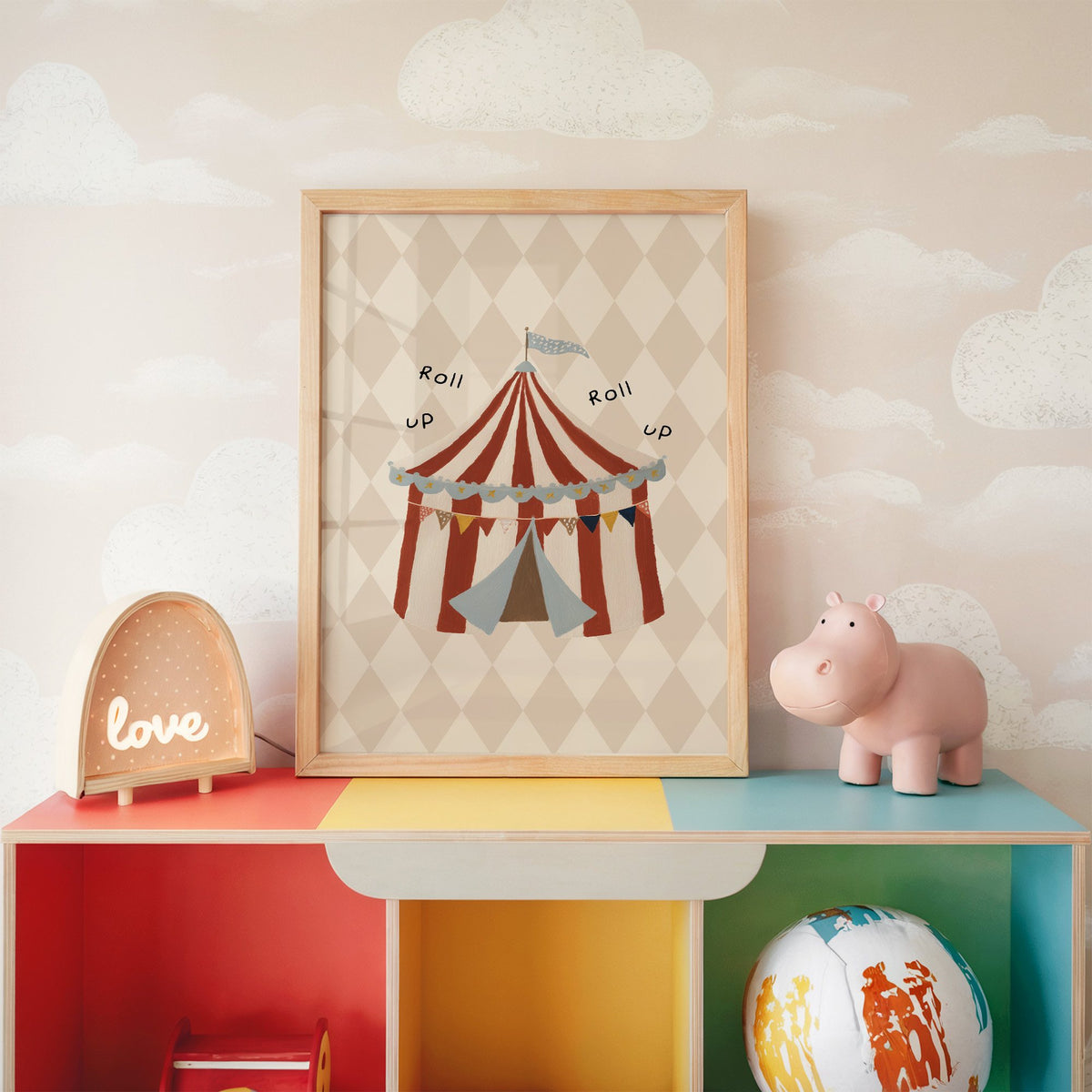 Roll up circus tent nursery print in an oak frame on a rainbow toy shelf against cloud wallpaper