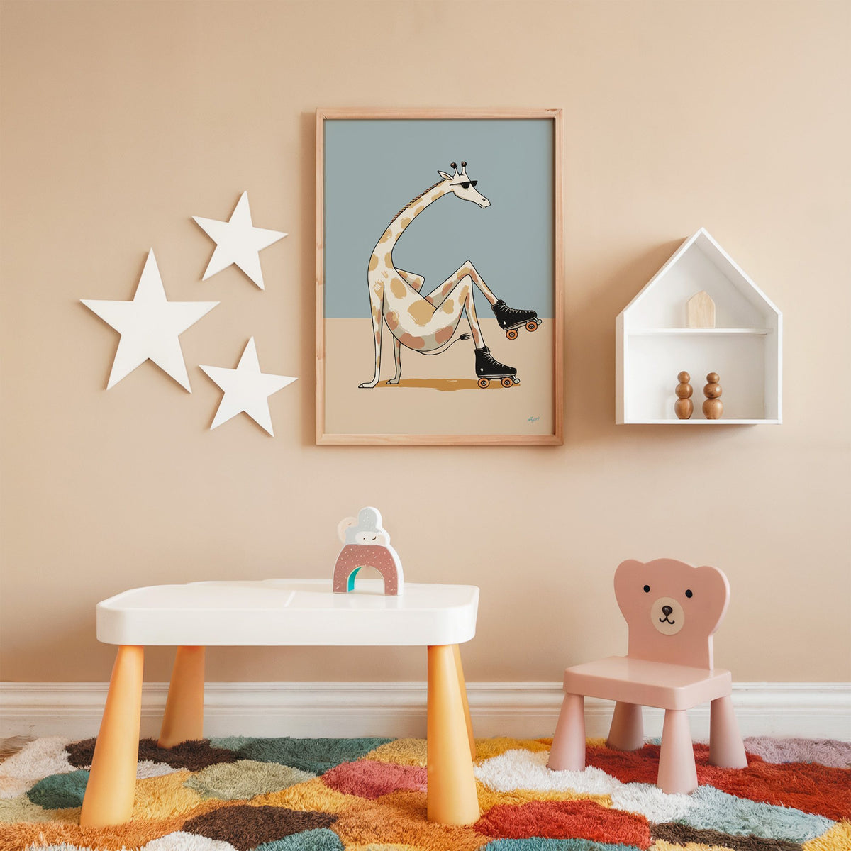Giraffe wearing roller skates nursery print in an oak frame on a peach wall above a kids table with wall stars