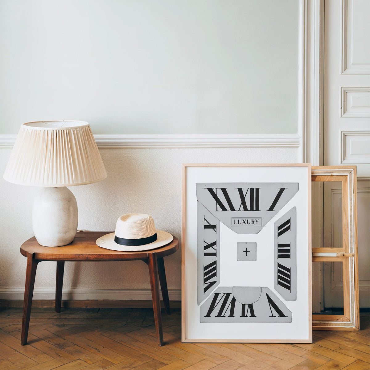 Broken Roman numeral clock dial graphic print in a pine frame on a wood floor beside a lamp and straw hat