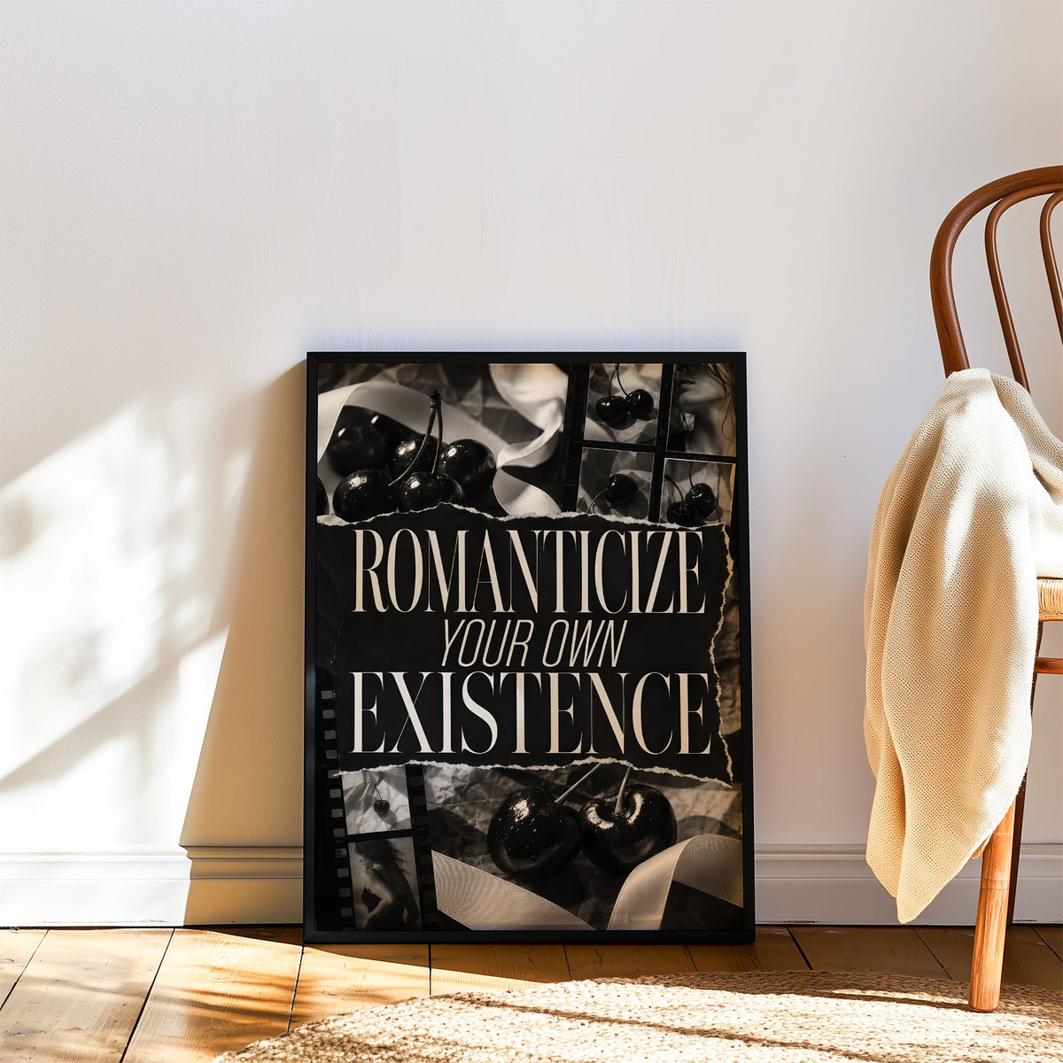Romanticize your own existence cherry collage print in a black frame leaning on a wood floor beside a bentwood chair