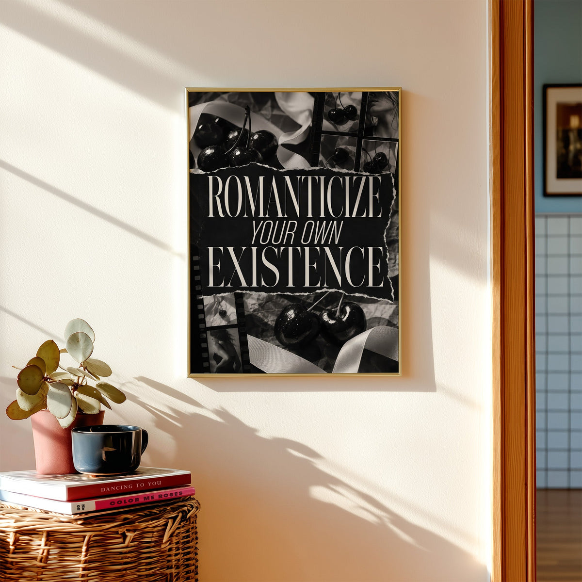 Romanticize your own existence cherry collage print shown in a gold frame above a wicker basket and stacked books