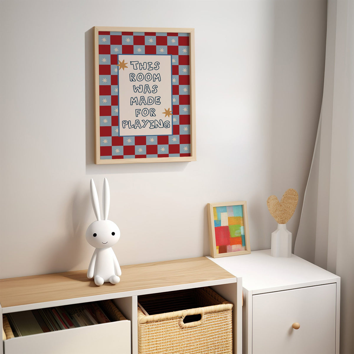 Room made for playing checkered nursery print in an oak frame above a kids cubby shelf with a woven basket and bunny lamp