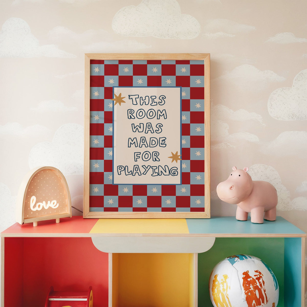 Room made for playing checkered nursery print in an oak frame on a rainbow toy shelf against cloud wallpaper