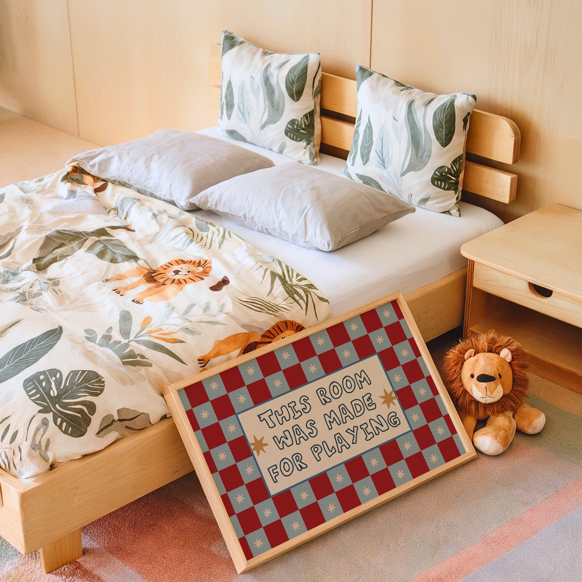 Landscape room made for playing checkered nursery print in an oak frame leaning on a kids bed by a lion plush