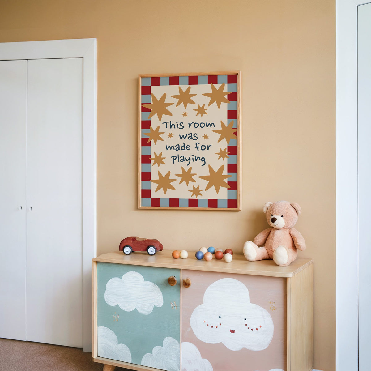 Room made for playing stars nursery print in an oak frame on a peach wall above a cloud-painted cabinet