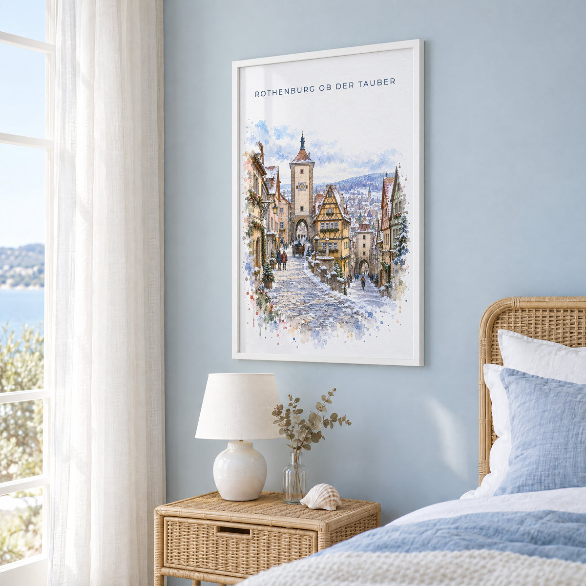 Rothenburg ob der Tauber watercolor print in a white frame on a pale blue wall beside a rattan bed in a coastal bedroom