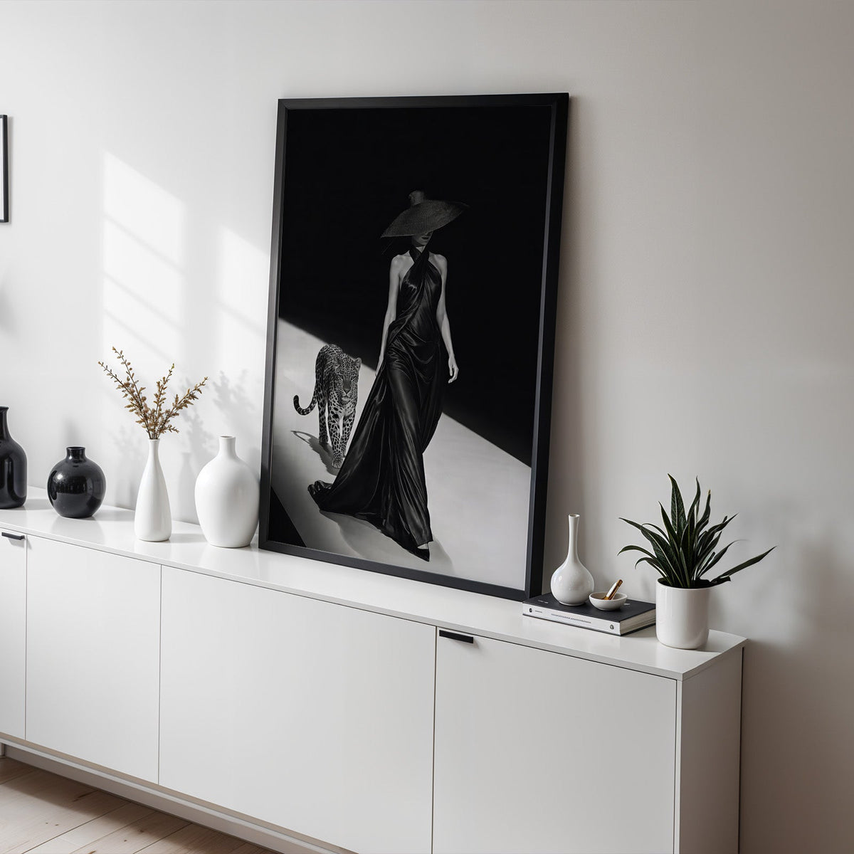 Woman in satin gown and wide hat with leopard print in a black frame on a white sideboard with black and white vases