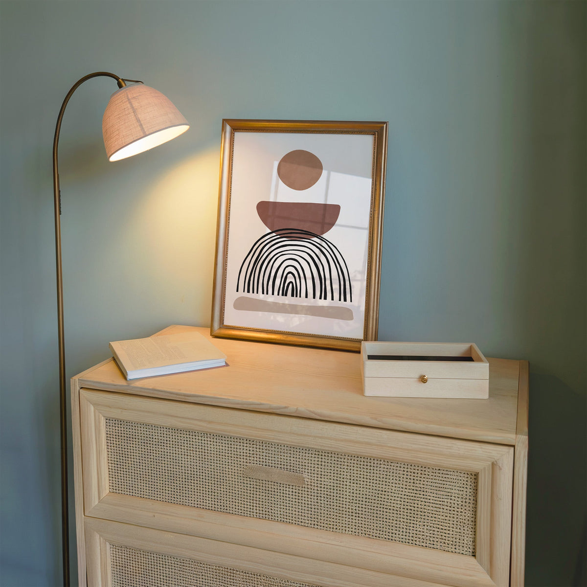 Rust bowl and black wobbly arch boho print shown in a gold frame on a cane dresser lit by a floor lamp