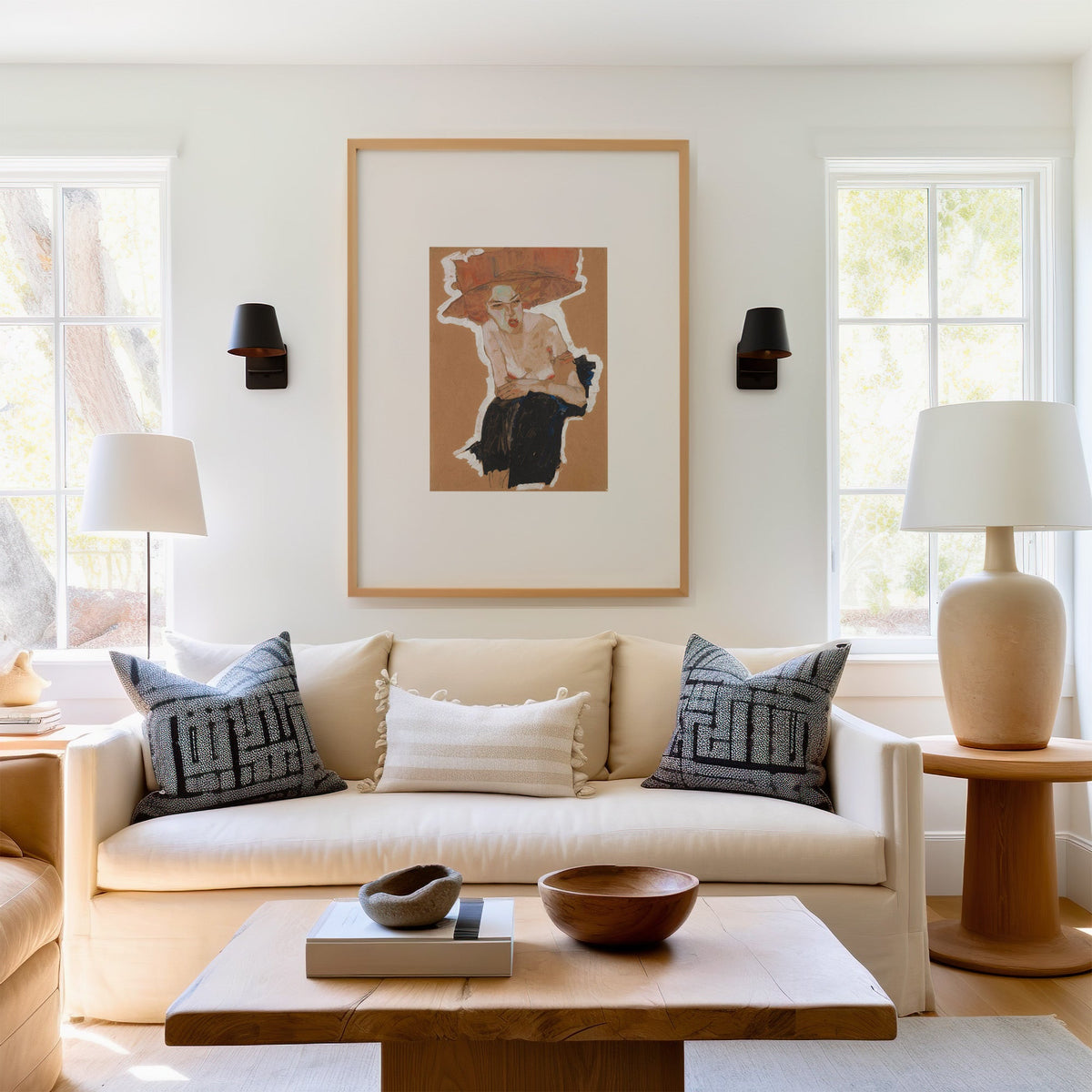 Rust hat woman gouache on kraft paper print in a light oak frame above a cream sofa between two black wall sconces