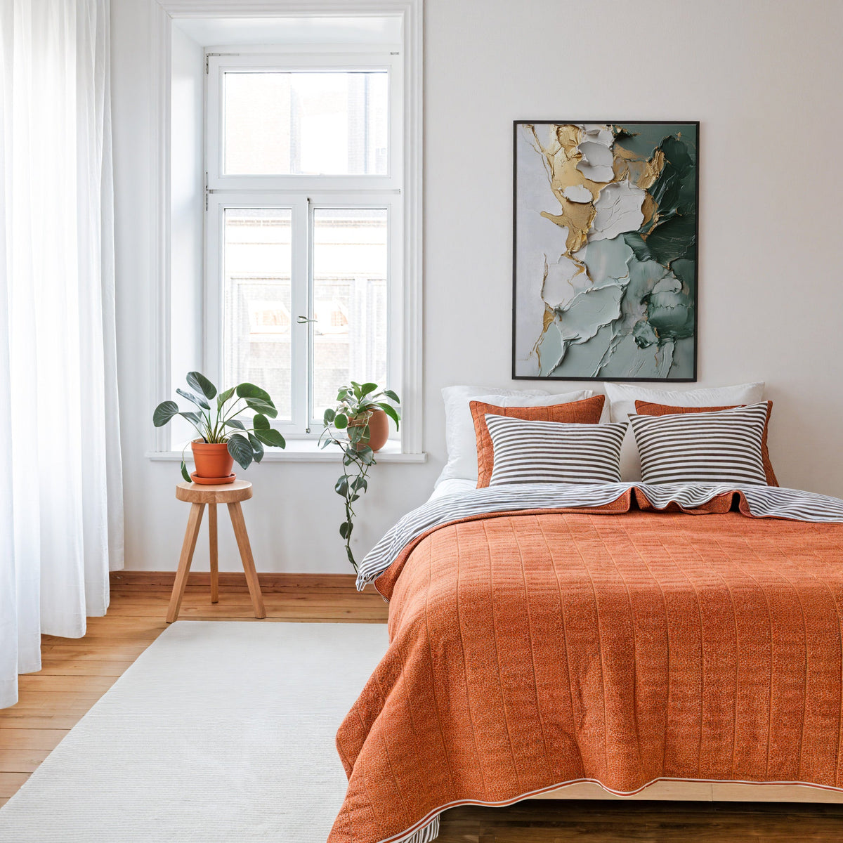 Sage green and gold impasto abstract print in a thin black frame above a bed with a rust orange quilt