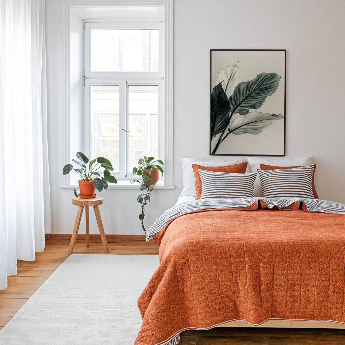 Sage green leaves abstract botanical print in a thin black frame above a bed with a rust orange quilt