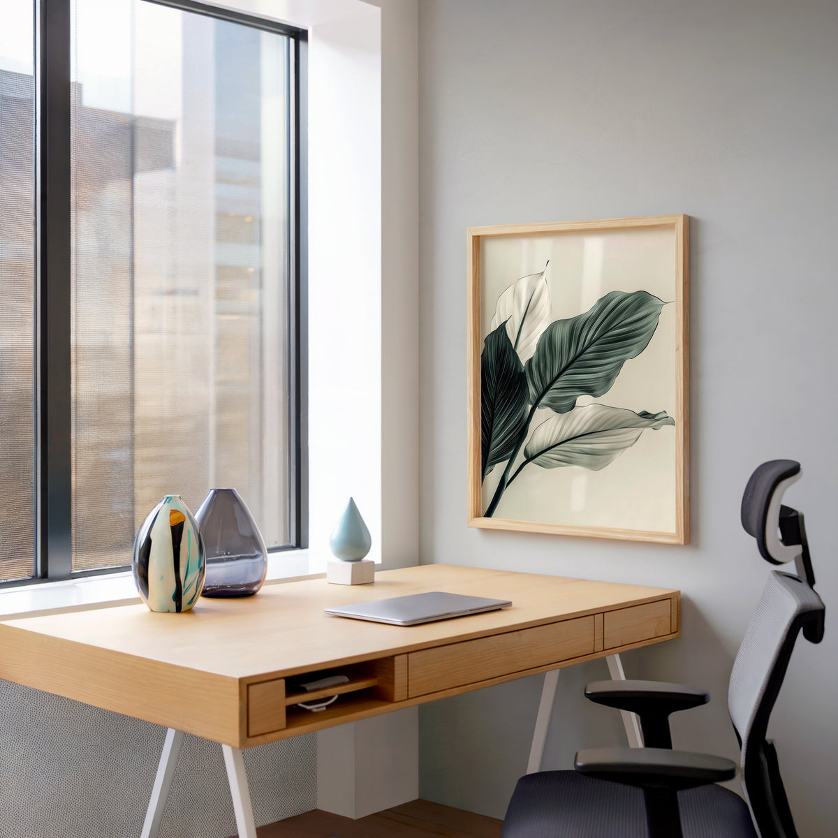 Sage green leaves abstract botanical print in a pale wood frame above a home office desk by a tall window