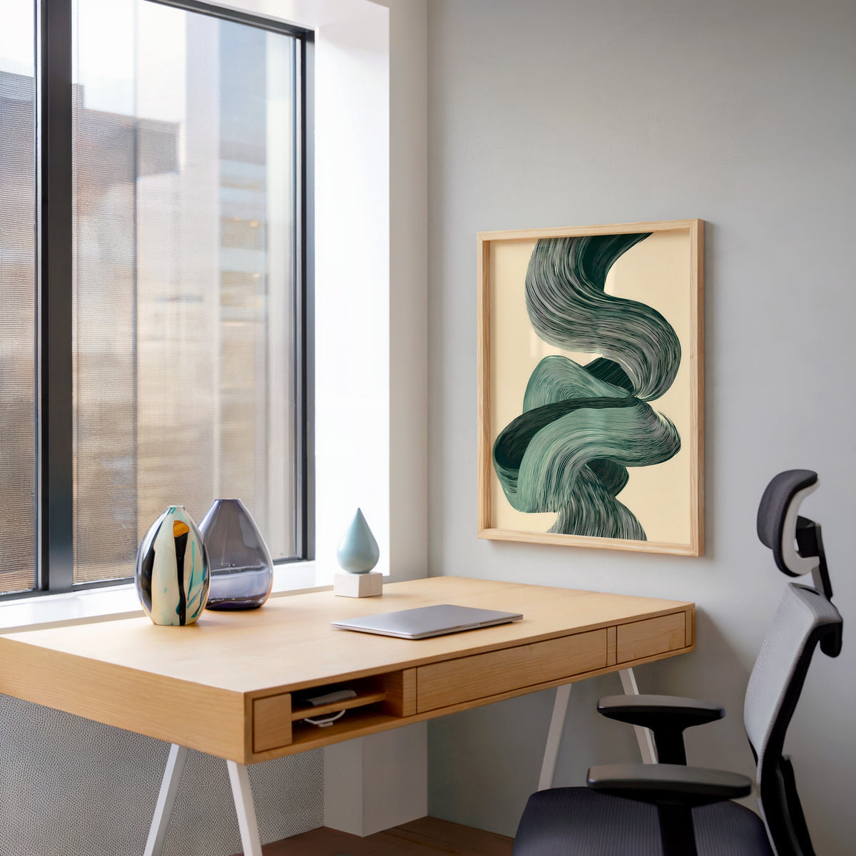 Sage green line ribbon swirl abstract print in a pale wood frame above a home office desk by a tall window
