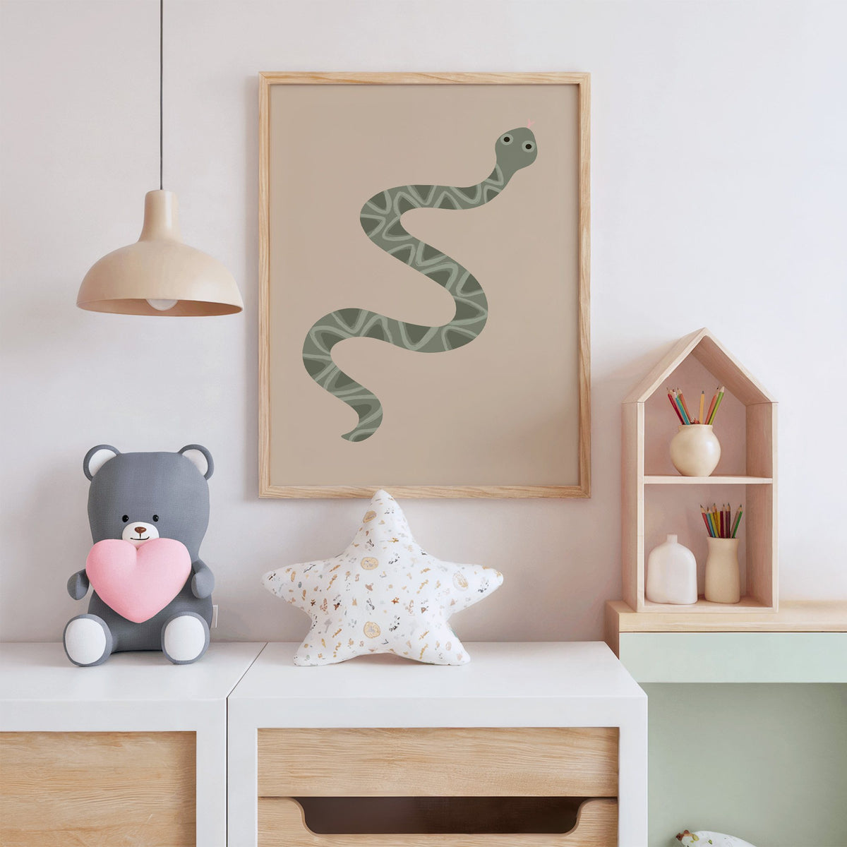 Sage green snake nursery print in an oak frame above a white dresser with a star pillow and house shelf