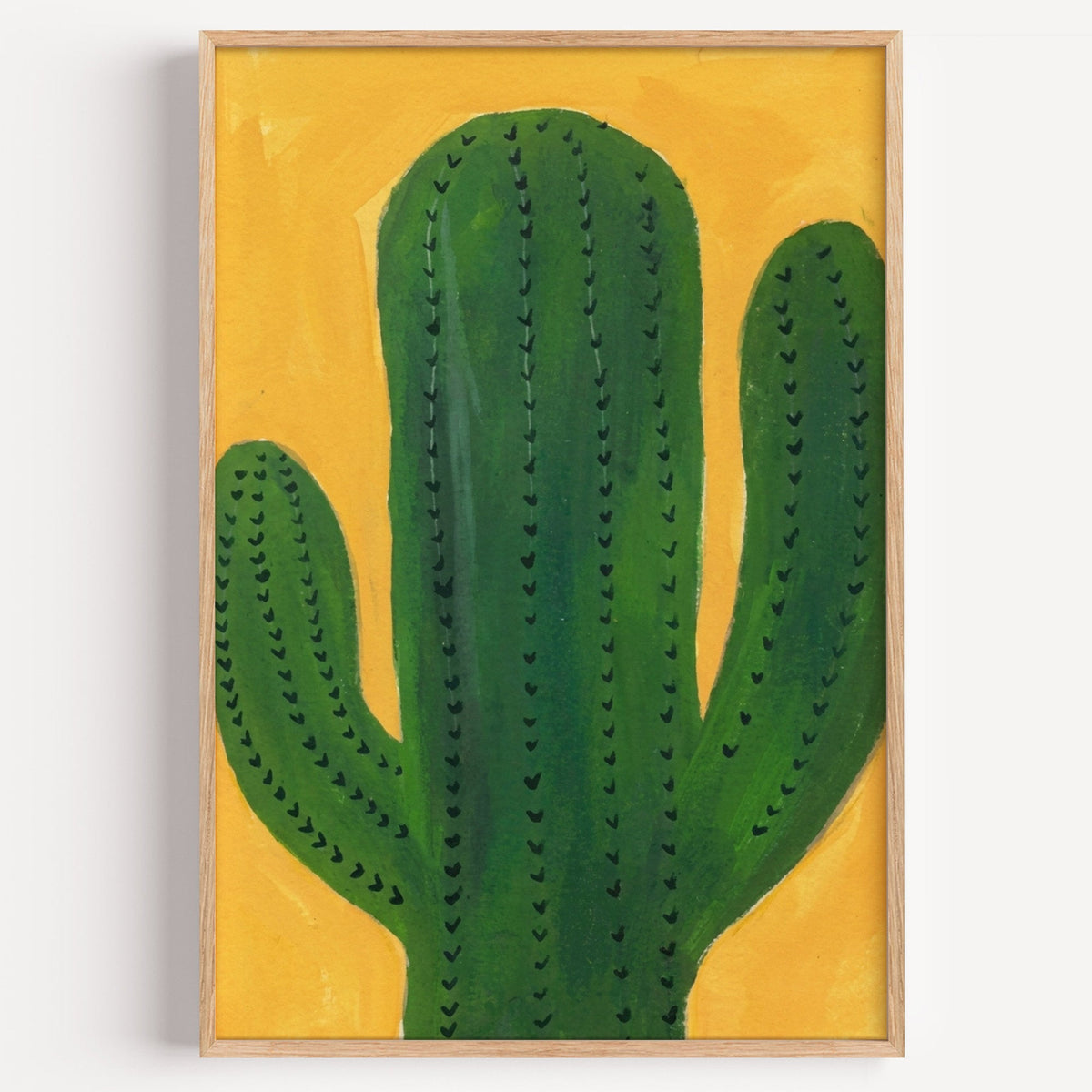 Green cactus on mustard print in a light oak frame on a plain white wall
