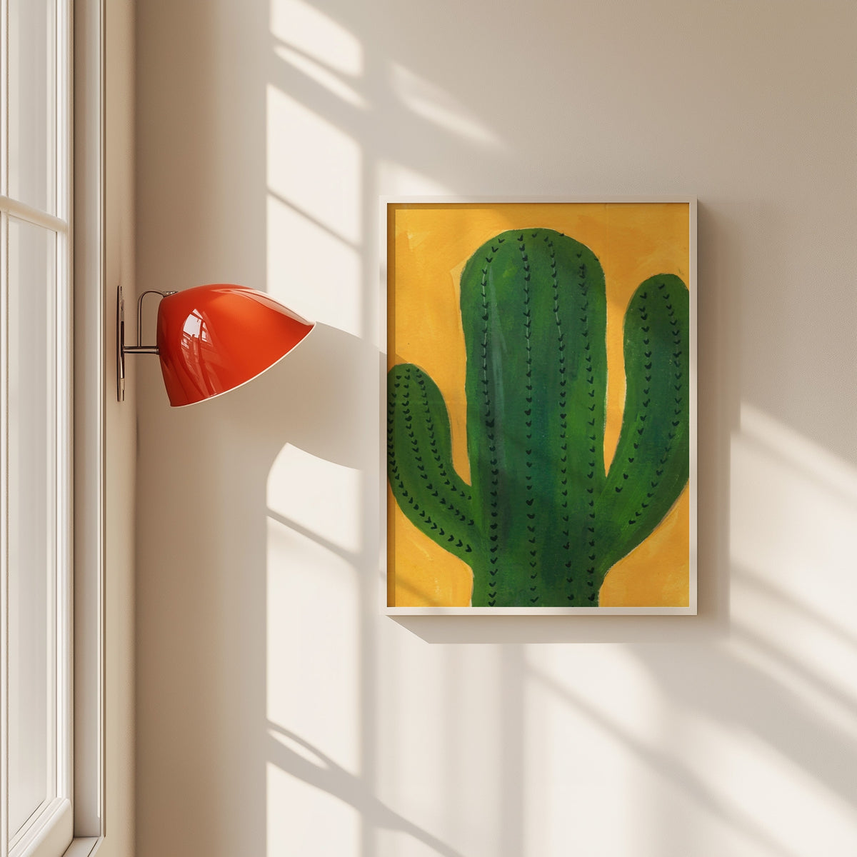 Green cactus on mustard print in a white frame beside a red wall sconce