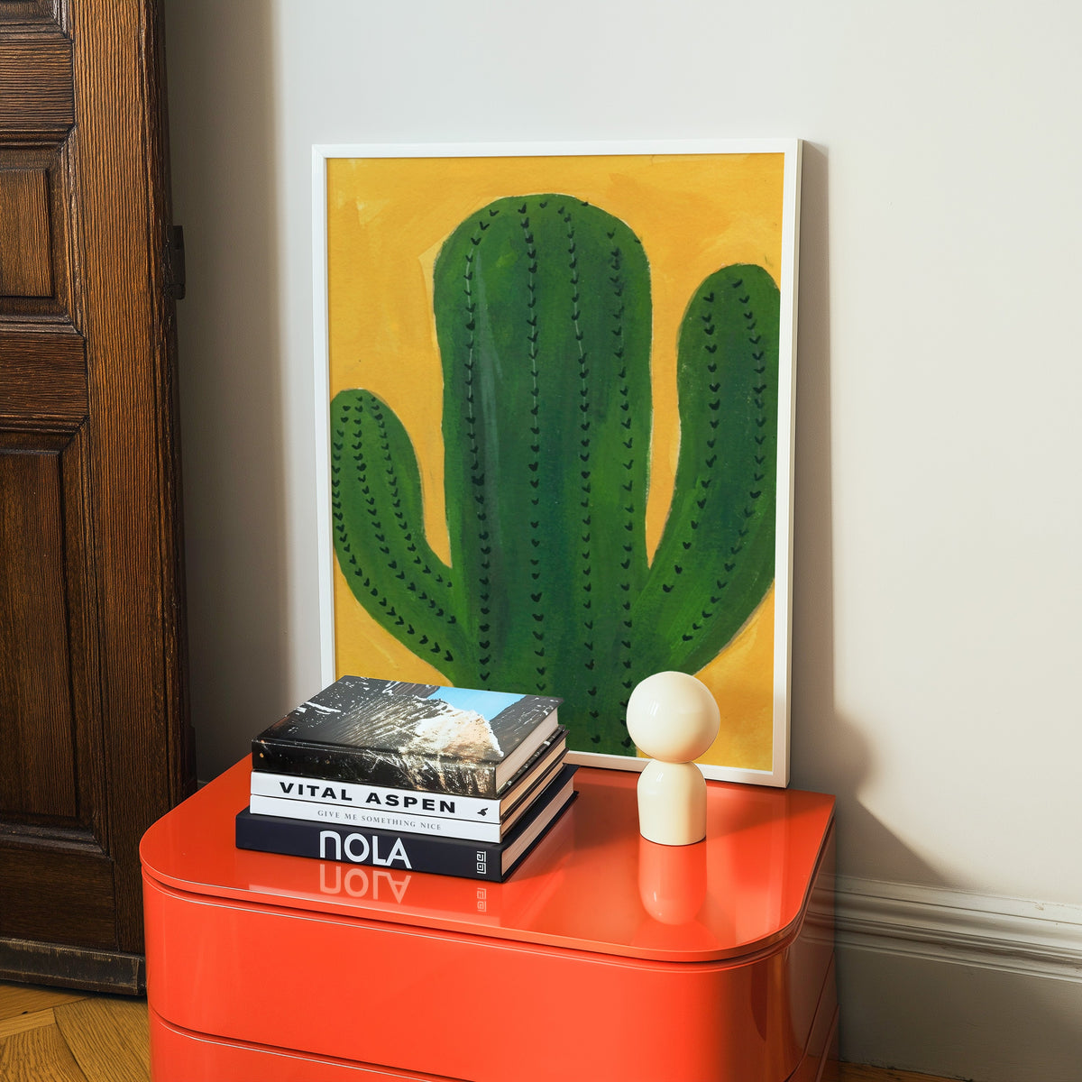 Desert cactus print in a white frame on a glossy orange cabinet with books