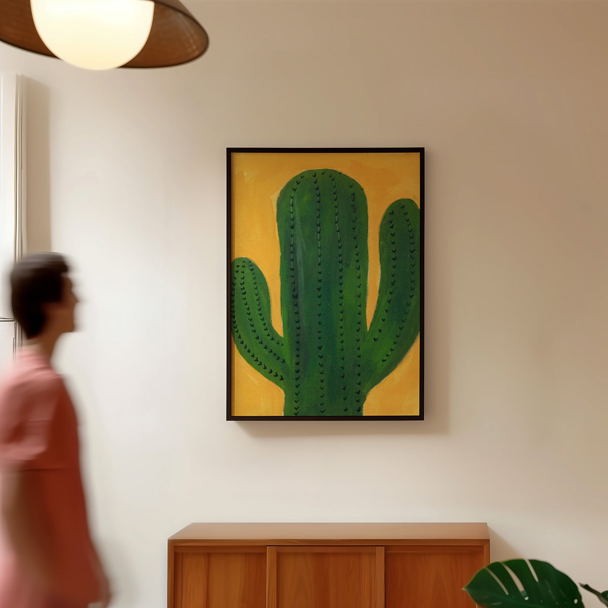 Mustard and green cactus print in a black frame in a hallway under a rattan pendant