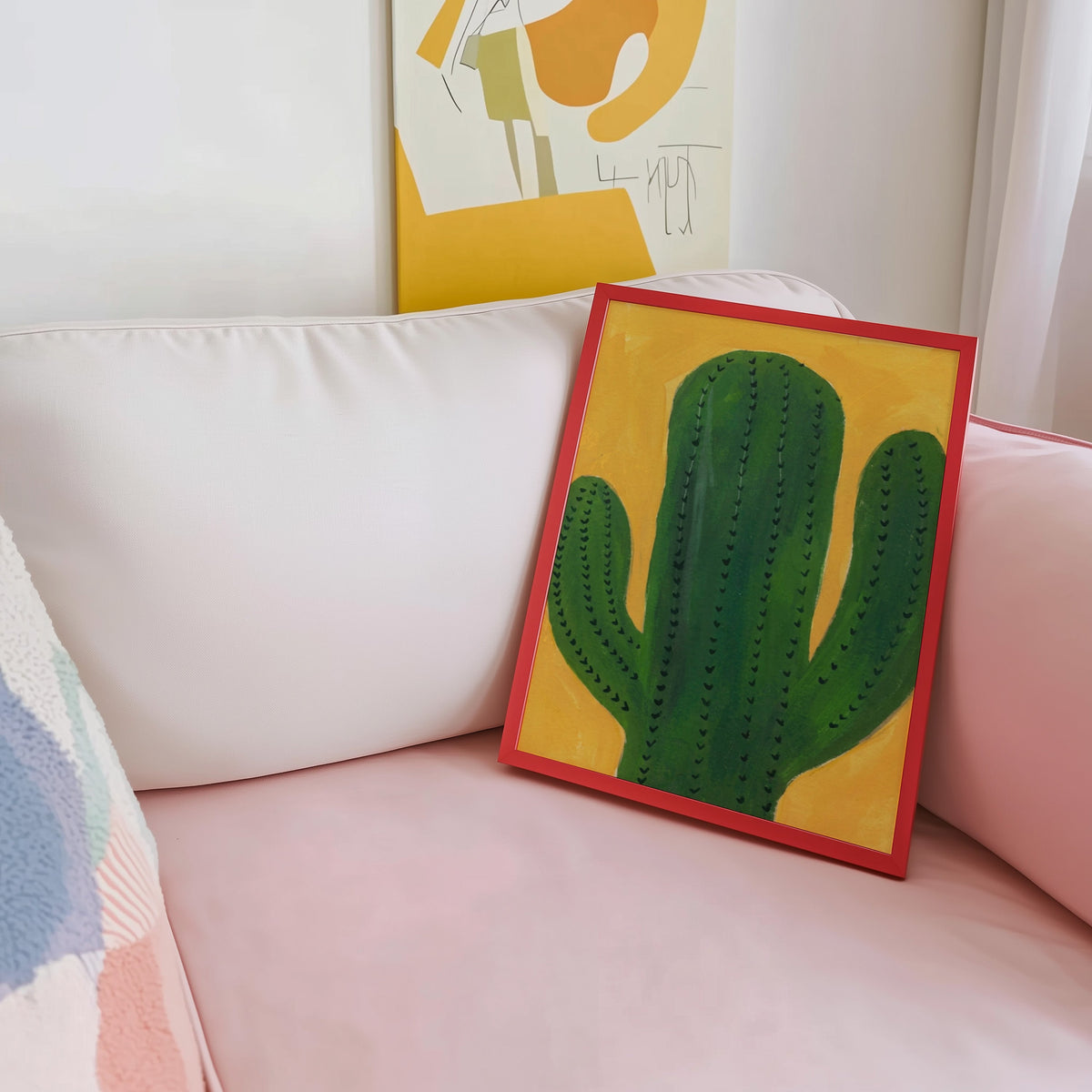 Boho cactus wall art print shown in a red frame leaning on a blush pink sofa