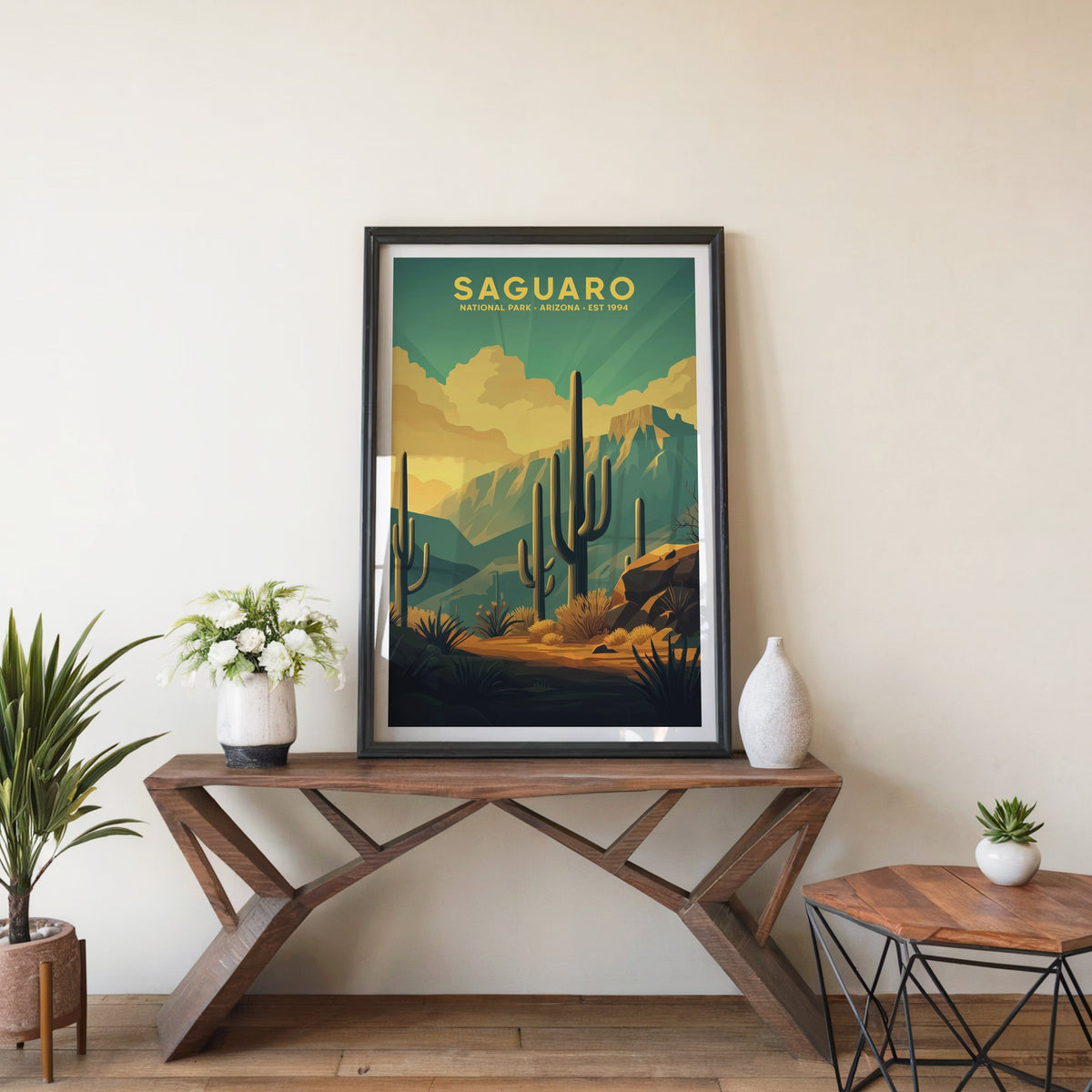 Saguaro poster in a black frame on an entryway console table beside white flowers and a yucca