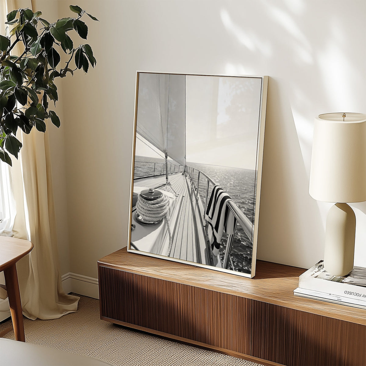 Sailboat deck with rope coil and striped towel print in a white frame on a walnut sideboard beside a ceramic lamp