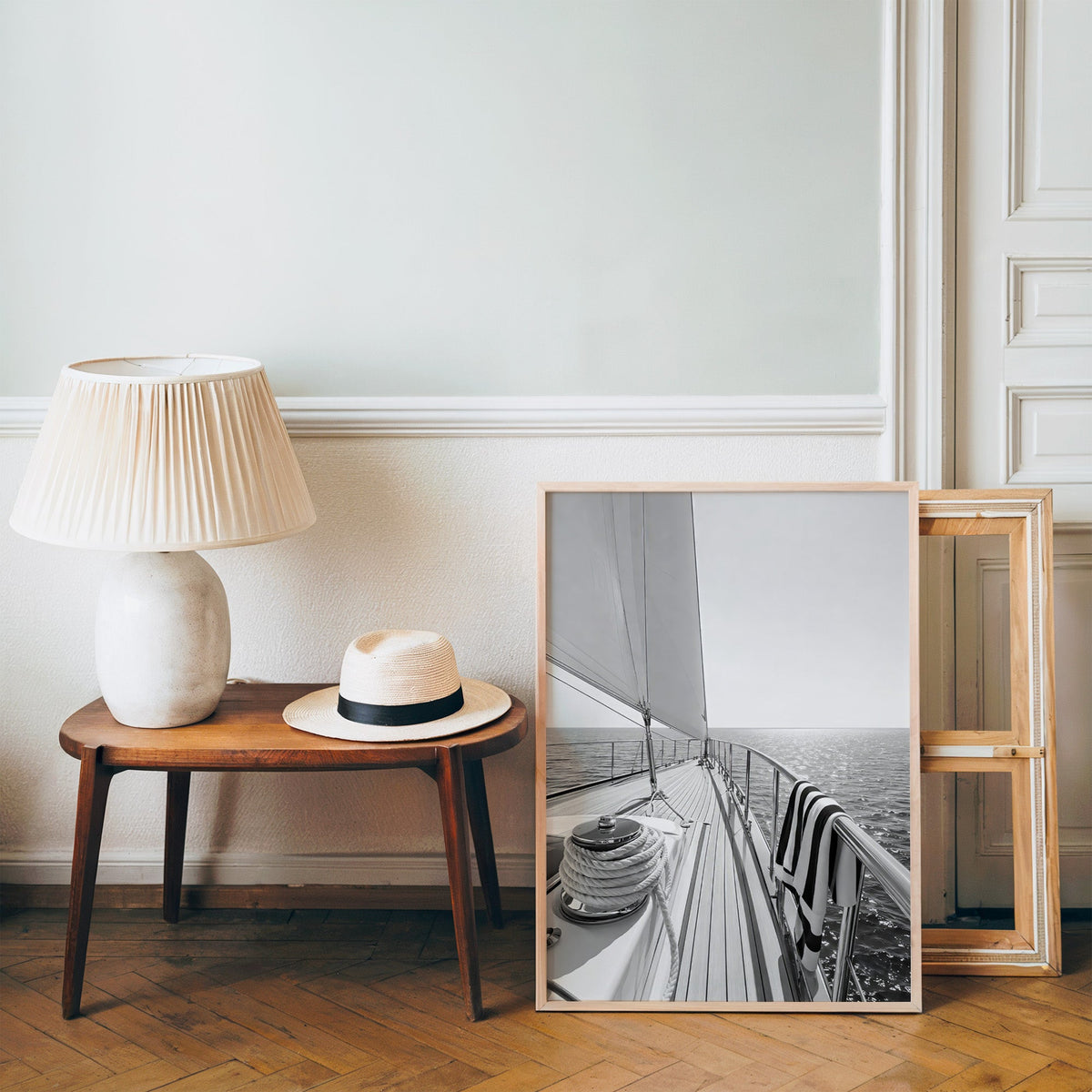 Sailboat deck with rope coil and striped towel print in a pine frame on a wood floor beside a lamp and straw hat