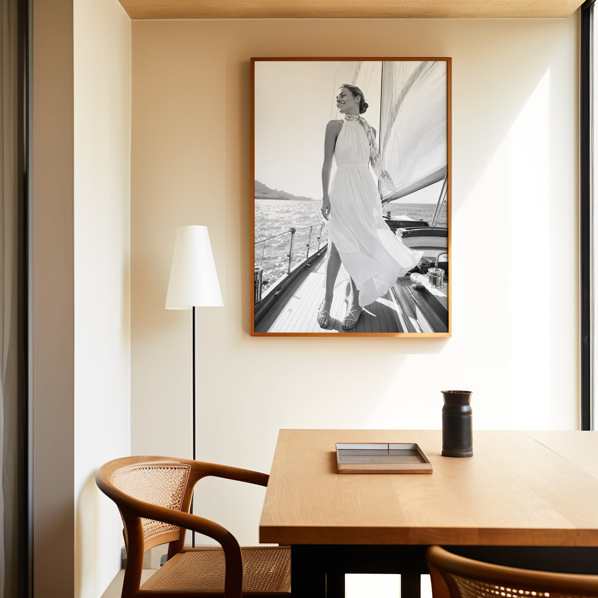 Black and white woman in white dress on sailboat print in an oak frame above a dining table and cane chair