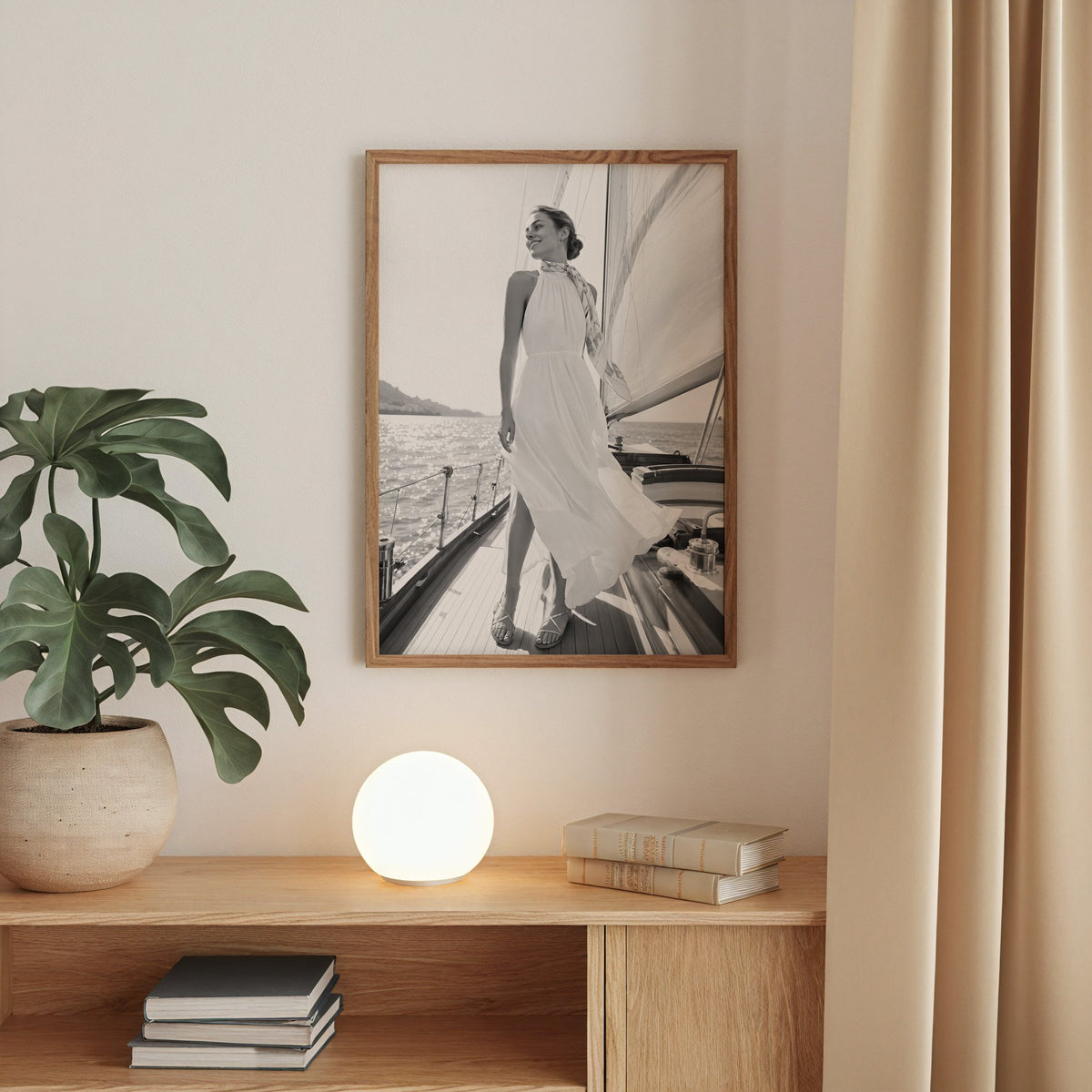 Black and white woman in white dress on sailboat print in a walnut frame above an oak cabinet with a glowing globe lamp