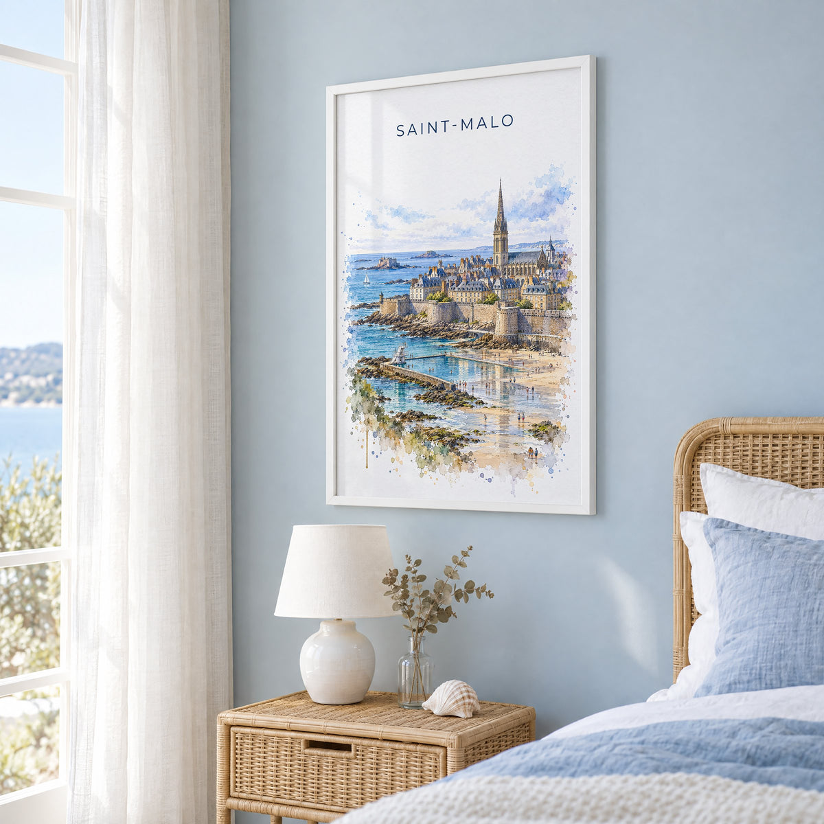 Saint-Malo watercolor print in a white frame on a pale blue wall beside a rattan bed in a coastal bedroom